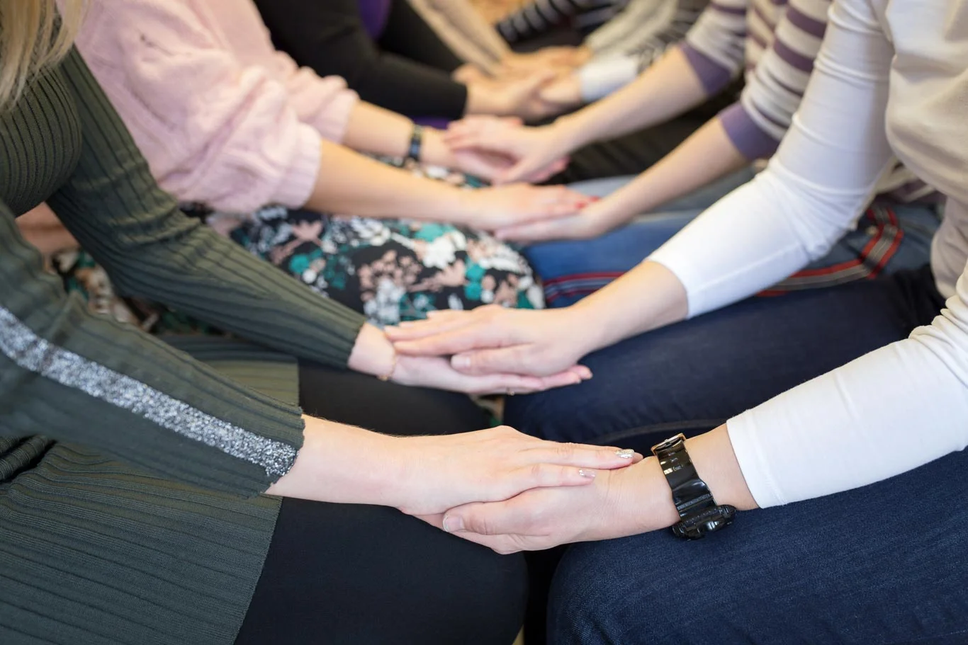 Ihmisiä istuu meditoimassa käsi kädessä.